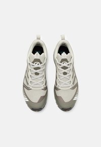 Grijze en beige sport schoenen met een gestructureerde mesh bovenkant, contrasterende strepen en platte veters. Heeft een trekband op de hiel.