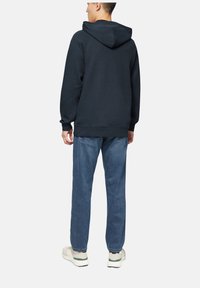 Felpa blu navy in una vestibilità comoda con un grande cappuccio. Abbinata a jeans azzurri e scarpe da ginnastica bianche con dettagli verdi.