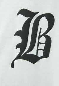 Tessuto bianco con un grande logo stilizzato "B" nero, con dettagli ornati e forme contrastanti, creando un design grafico audace.