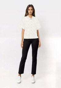 White short-sleeve button-up blouse with eyelet pattern, paired with black fitted trousers and white sneakers.