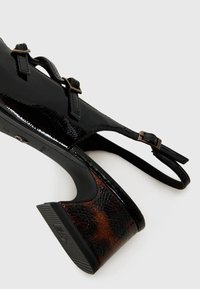 Schwarze lackleder Slingback-Pumps mit zwei verstellbaren Riemen, die einen strukturierten braunen gemusterten Absatz für zusätzlichen Kontrast bieten.