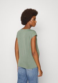 Camiseta verde de manga curta em tecido suave com um corte descontraído, apresentando um decote redondo e uma barra curvada, combinada com jeans azul claro.