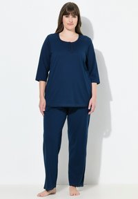 Tmavě modrý relaxační komplet sestávající z topu s krátkým rukávem a knoflíkovými detaily a krajkovými akcenty, doplněný o odpovídající kalhoty. Jemná textura látky.