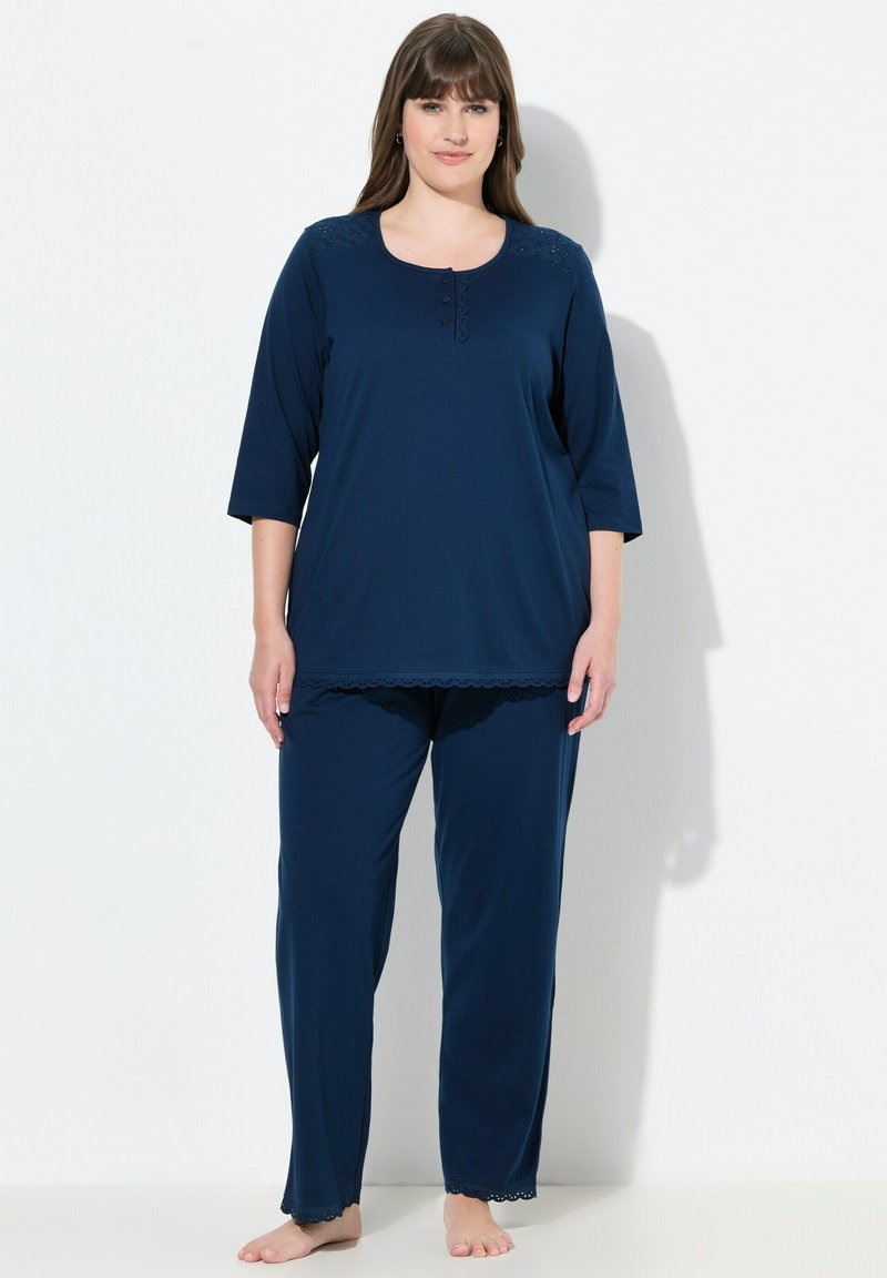 Tmavě modrý relaxační komplet sestávající z topu s krátkým rukávem a knoflíkovými detaily a krajkovými akcenty, doplněný o odpovídající kalhoty. Jemná textura látky.