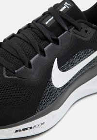 Chaussure de sport noire avec une tige en maille texturée, un swoosh blanc de Nike et une semelle en caoutchouc noire arborant le logo "AIR ZOOM".