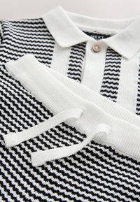 Polo de punto en blanco y negro con cuello blanco y botón, combinado con pantalones de punto a juego con cintura ajustable blanca con cordón.