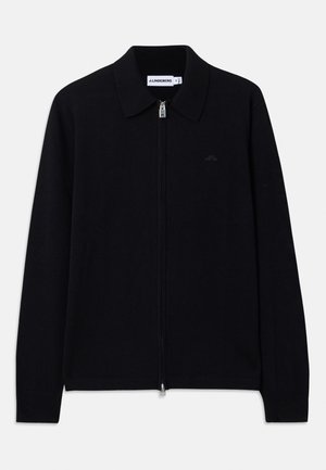 Pull zippé noir avec un col, manches longues, poignets côtelés et un logo discret sur la poitrine. Matière tricotée douce.