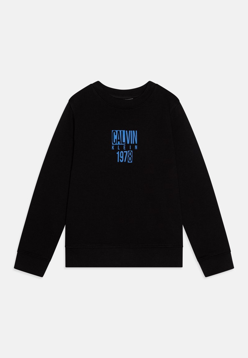 Črna majica z dolgimi rokavi z modrim grafičnim tiskom, ki na sprednji strani nosi napis "CALVIN KLEIN 1978". Ima rebraste manšete in obliko kroga pri vratu.