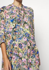 Robe florale en tissu léger présentant des fleurs roses, bleues et jaunes sur fond vert. Détails en boutons et jupe plissée.