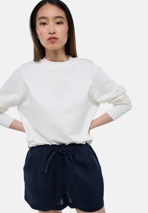 Sweatshirt blanc à col rond avec des manches longues, associé à un short bleu marine foncé avec une taille élastique et un cordon de serrage.