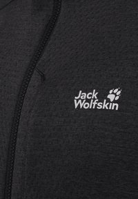 Zwarte fleecejas met een getextureerd patroon, ritssluiting en een wit "Jack Wolfskin"-logo met pootafdrukdetail.