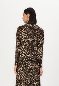 Langermet topp med leopardmønster, mykt stoff med brune og svarte flekker på en beige bakgrunn, avslappet passform med buet kant.