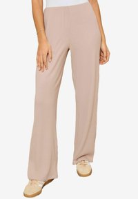 Wijdvallende broek in lichtbeige, gemaakt van ribbelstof. Geladde textuur met een elastische tailleband, gestyled met lichtbeige sneakers.