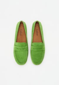Zelené semišové loafers s prešitým dizajnom, s malým akcentovým popruhom a hnedým vnútorným podšívkou pre pohodlie.