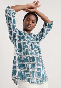 Aqua en witte blouse met patroon, voorzien van een V-hals, driekwart mouwen en een losse fit met een abstracte penseelstrekenontwerp.