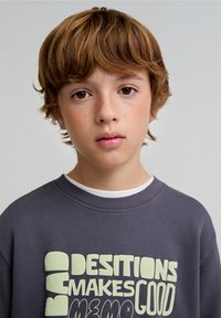 Grijze sweatshirt met vet, lichtgroene tekst: "SLECHTE BESLISSINGEN MAKEN GOEDE HERINNERINGEN." Zachte stof met geribbelde halslijn en manchetten.
