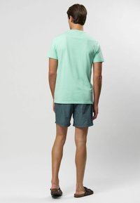 Mentolovo zelená košeľa s krátkym rukávom, z ľahkej látky, v kombinácii s tehlovo modrými a bielymi pruhovanými šortkami a tmavohnedými sandálmi. Jednoduchý dizajn a strih.