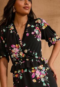 Mustardate mustarhõlmikega must lilleline kleit, kus on roosa, kollane ja roheline lillemuster, volangkaeluse ja -varrukatega, ning peplum talje detail.