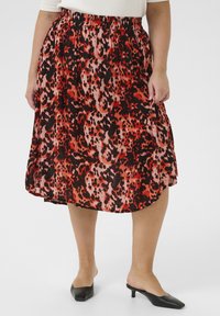 Jupe imprimée léopard rouge et noire avec une taille élastique, longueur genoux, fabriquée en tissu léger, présentant une silhouette fluide et plissée.