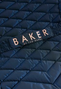 Marineblaues gestepptes Gewebe mit einem Diamantmuster; verfügt über ein schwarzes Gummiband mit "BAKER by TED BAKER" in roségoldener Schrift.
