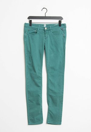 Turkooise slim-fit jeans met knoop- en ritssluiting, voor- en achterzakken, hangend aan een zwarte plastic hanger tegen een witte achtergrond.