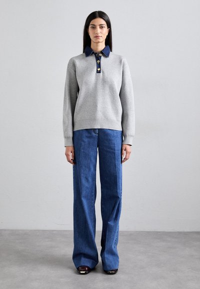 Felpa grigia con colletto blu e bottoni dorati, abbinata a jeans blu a gamba larga, con una texture liscia e una vestibilità sartoriale.