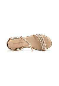 Sandaales strappy de oro rosa con tiras trenzadas, plantilla en color beige y hebilla en el tobillo. Textura suave con suela plana y diseño minimalista.