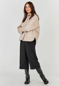 Beež paksu voodriga jakk, millel on kõrge krae, on kombineeritud mustade laia säärega pükstega ja põlvini ulatuvate mustade saapatega; sile kangas ja mugav lõige.