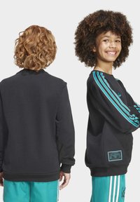 Sweatshirt nero con strisce turchesi e dettagli dell'etichetta. Presenta un collo a giro e polsini a coste, abbinato a pantaloni sportivi turchesi coordinati.