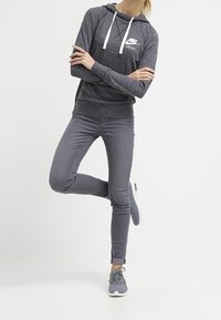 Grå Nike-hoodie med en vit logotyp, i kombination med slim fit grå jeans och grå sneakers. Hoodien har en dragsko i huvan och ribbade ärmslut.