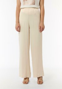 Beżowe spodnie o szerokich nogawkach z gładkiego materiału, z elastycznym pasem i bocznymi kieszeniami, w połączeniu z pasującymi sandałami na paski.