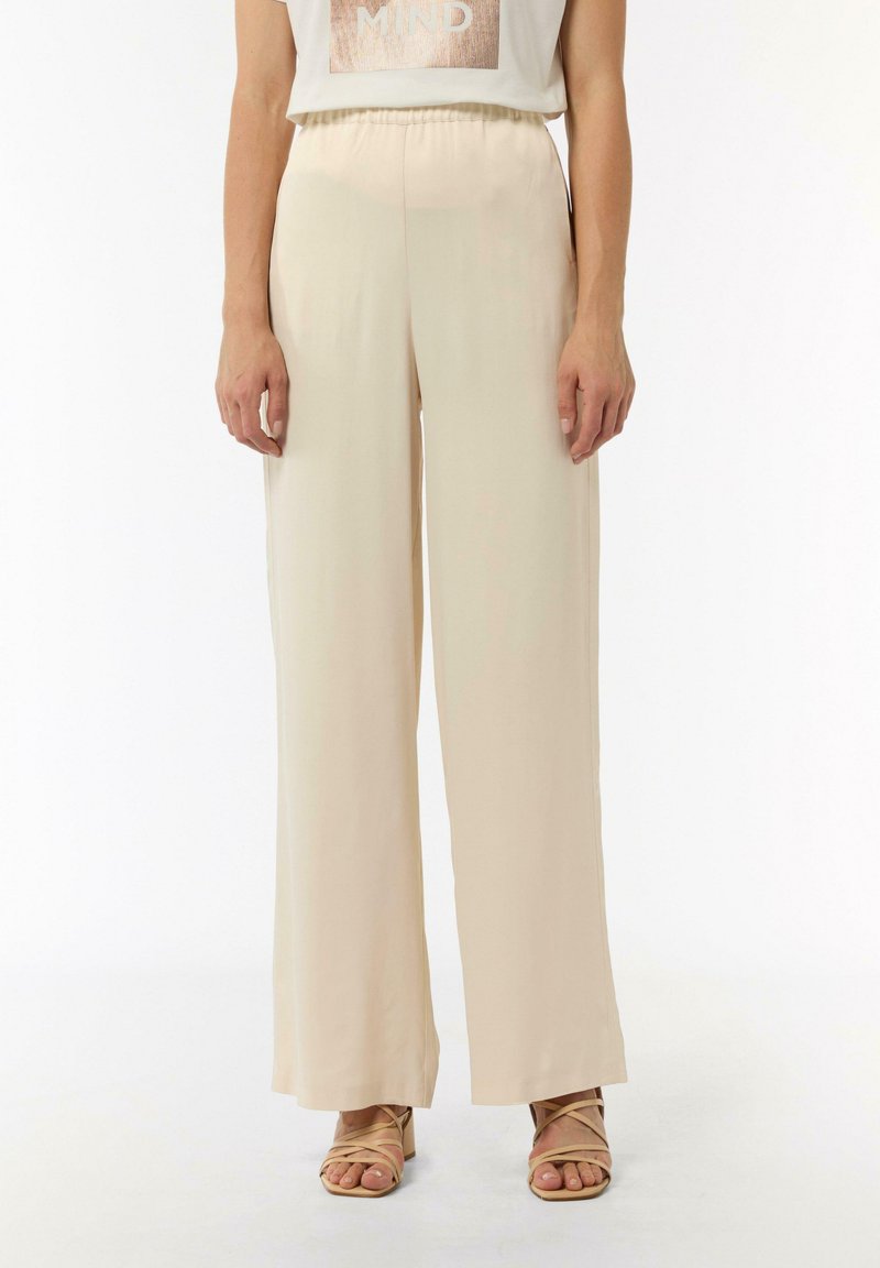 Beżowe spodnie o szerokich nogawkach z gładkiego materiału, z elastycznym pasem i bocznymi kieszeniami, w połączeniu z pasującymi sandałami na paski.