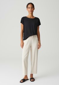 Zwart T-shirt met korte mouwen, relaxte pasvorm; crèmekleurige broek met drawstring; platte zwarte sandalen met kruissluitingen; gladde stof; minimalistisch ontwerp.