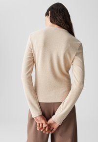 Cremefarbenes, geripptes Langarmoberteil mit Rundhalsausschnitt, figurbetonter Silhouette und strukturiertem Stoff. Keine sichtbaren Verschlüsse oder Muster.