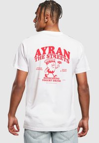 T-shirt en coton blanc avec un texte graphique rouge au dos : "AYRAN THE STREETS", accompagné d'un personnage joyeux de boisson au yaourt et de détails.