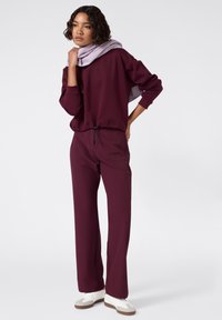 Sudadera burdeos con dobladillo ajustable, combinada con pantalones a juego, acentuada por una bufanda de color púrpura claro y zapatos blancos. Textura suave.