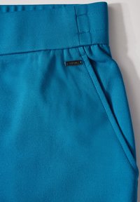 Blauwe stof met een gladde textuur, voorzien van een brede tailleband, gestikte details en een klein metalen label met de tekst "Cecil."