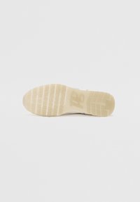 Sko såle med en teksturert gummioverflate i beige med lette spor, merkevarer synlig nær hælen, og en avrundet tådesign.