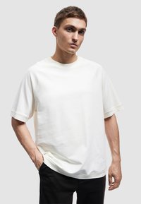 Helles beige Sweatshirt mit kurzen Ärmeln, Raglanärmeln, geripptem Rundhalsausschnitt und lockerer Passform. Glatte Textur, minimalistisches Design.