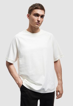 Helles beige Sweatshirt mit kurzen Ärmeln, Raglanärmeln, geripptem Rundhalsausschnitt und lockerer Passform. Glatte Textur, minimalistisches Design.