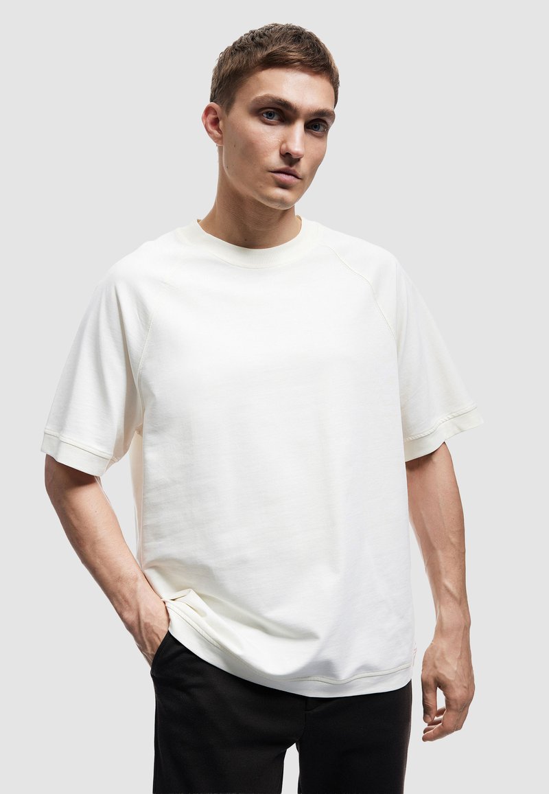 Helles beige Sweatshirt mit kurzen Ärmeln, Raglanärmeln, geripptem Rundhalsausschnitt und lockerer Passform. Glatte Textur, minimalistisches Design.