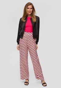 Zwarte satijnen bomberjack, felroze geribbelde top, witte broek met een roze en zwart hartpatroon, en zwarte sandaaltjes met bandjes.