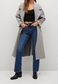 Gray wool coat with lapels over a black cropped top. Blue high-waisted jeans and black heeled ankle boots complete the look.