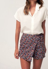 Valkoinen lyhythihaisen pusero yhdistettynä tummansiniseen kukkakietaisuhameeseen, jossa on punaisia, valkoisia ja sinisiä kukkia teksturoidulla kankaalla.