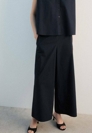 Culottes negras de corte ancho hechas de algodón, con cintura alta y bolsillos laterales, combinadas con un top sin mangas a juego.