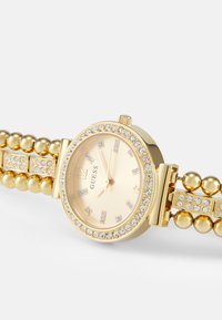 Gold wristwatch with a round case, crystal-embellished bezel, and beads on the band. Dial features a light gold face and gold hour markers.