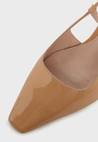 Chaussure slingback en cuir verni nude brillant, à bout pointu, avec une bride basse et des coutures visibles autour de l'ouverture.