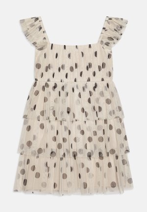 Vestido de niña pequeña en tul crema con lunares negros, con tirantes con volantes y un diseño en capas. Textura ligera y transparente.