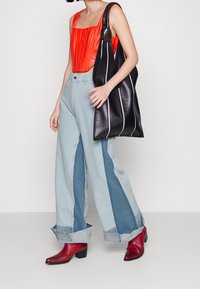 Punainen laskostettu crop-top yhdistettynä leveisiin vaaleansinisiin farkkuihin, joissa on tummansinista tilkkutyötä. Musta kangaskassi valkoisilla raidoilla ja punaiset nilkkurit.