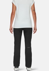 Svarta friluftsbukser med vinklade sömmar, elastiskt material och logodetaljer. I kombination med en ljusgrå åtsittande topp som är synlig bakifrån.